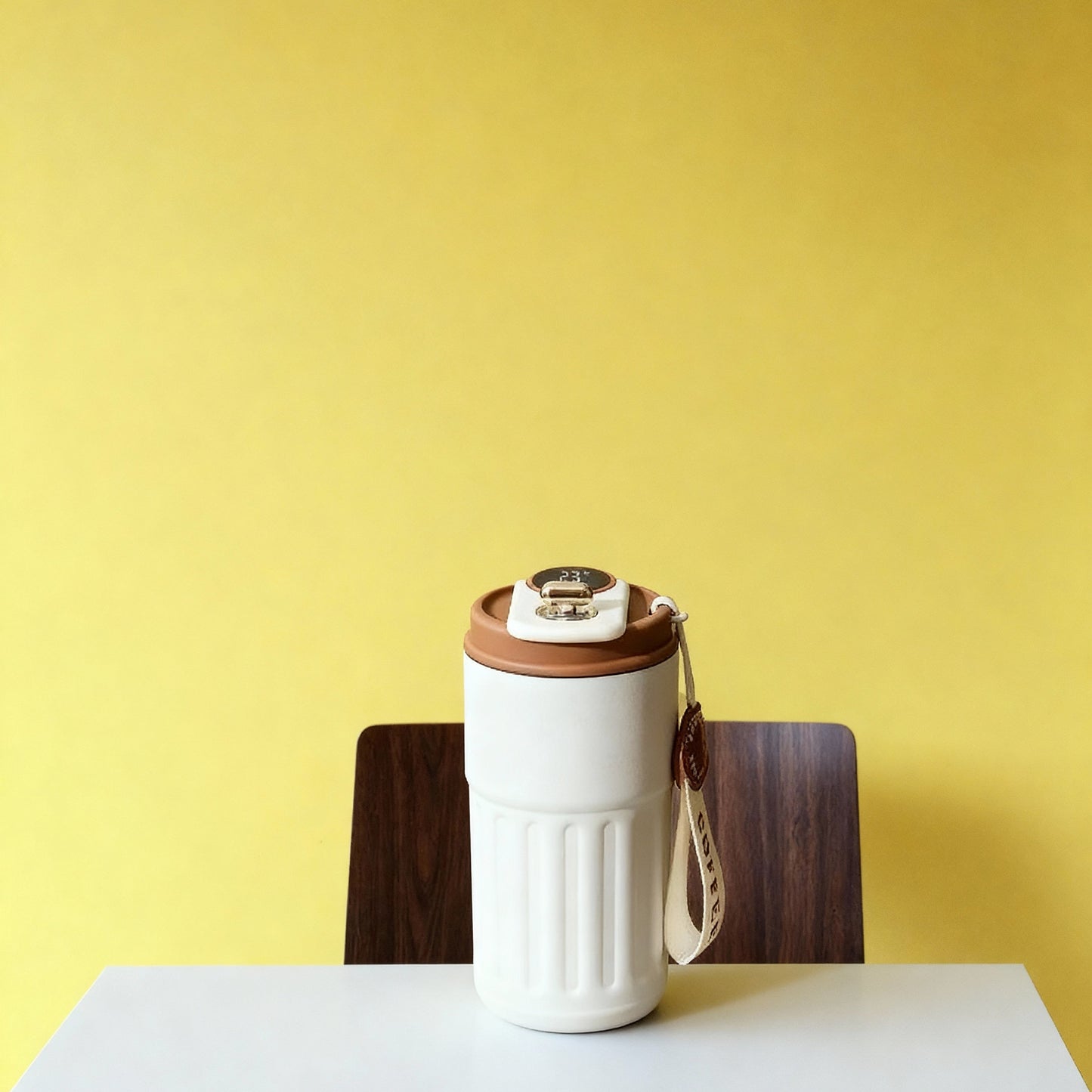 White travel mug with brown lid on a white table against a yellow wall