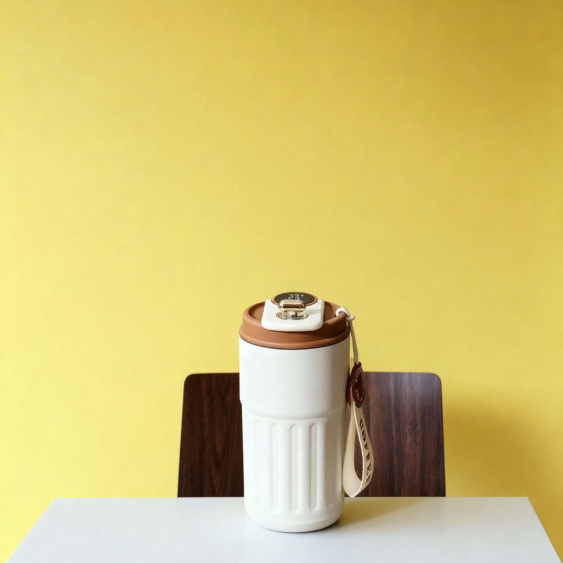 White travel mug with brown lid on a white table against a yellow wall