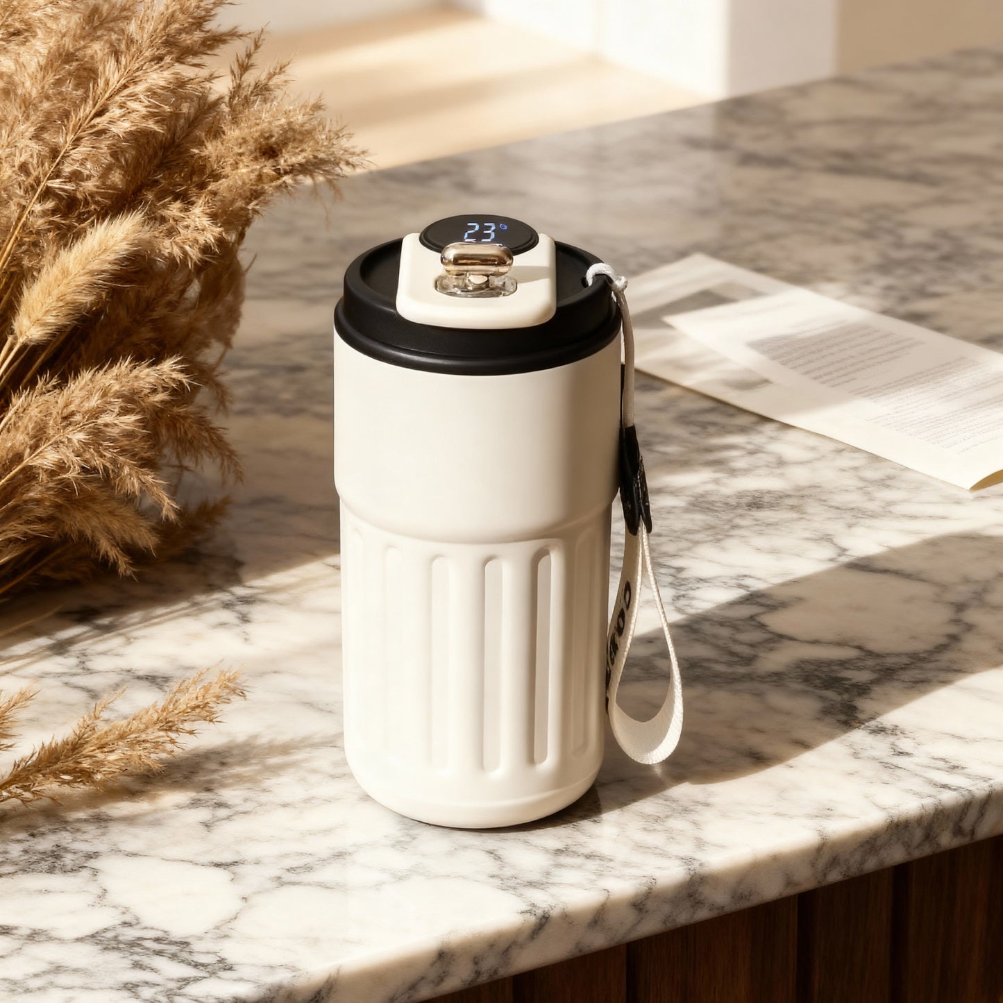 White travel mug with black lid on a marble surface with dried plants and newspaper.
